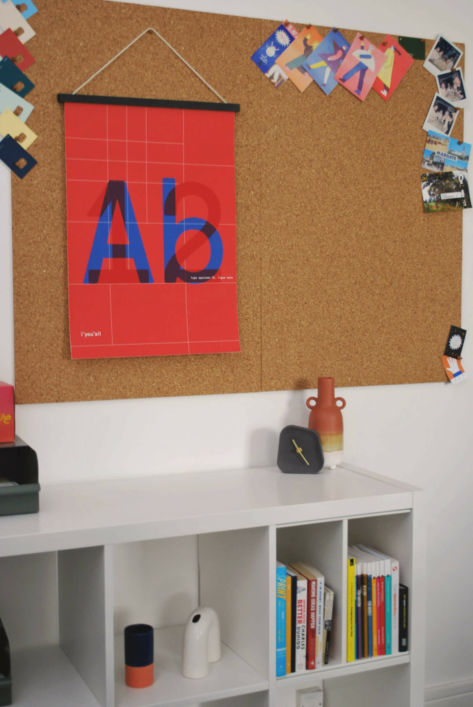 Corkboard with colorful posters, books, and decor items on a white shelf for a creative office space.