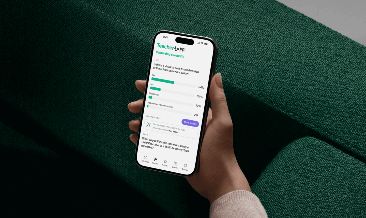 Person holding a phone displaying survey results on school behavior policy, green fabric background.